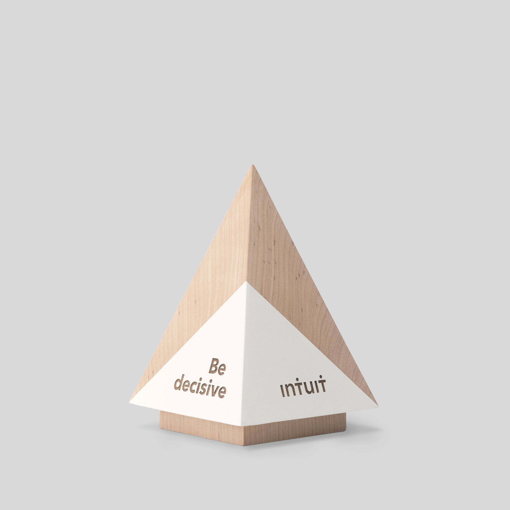 Geometria Award Pyramis: a wooden pyramid with a white triangle and engraved black text, showcasing minimalist design and craftsmanship.