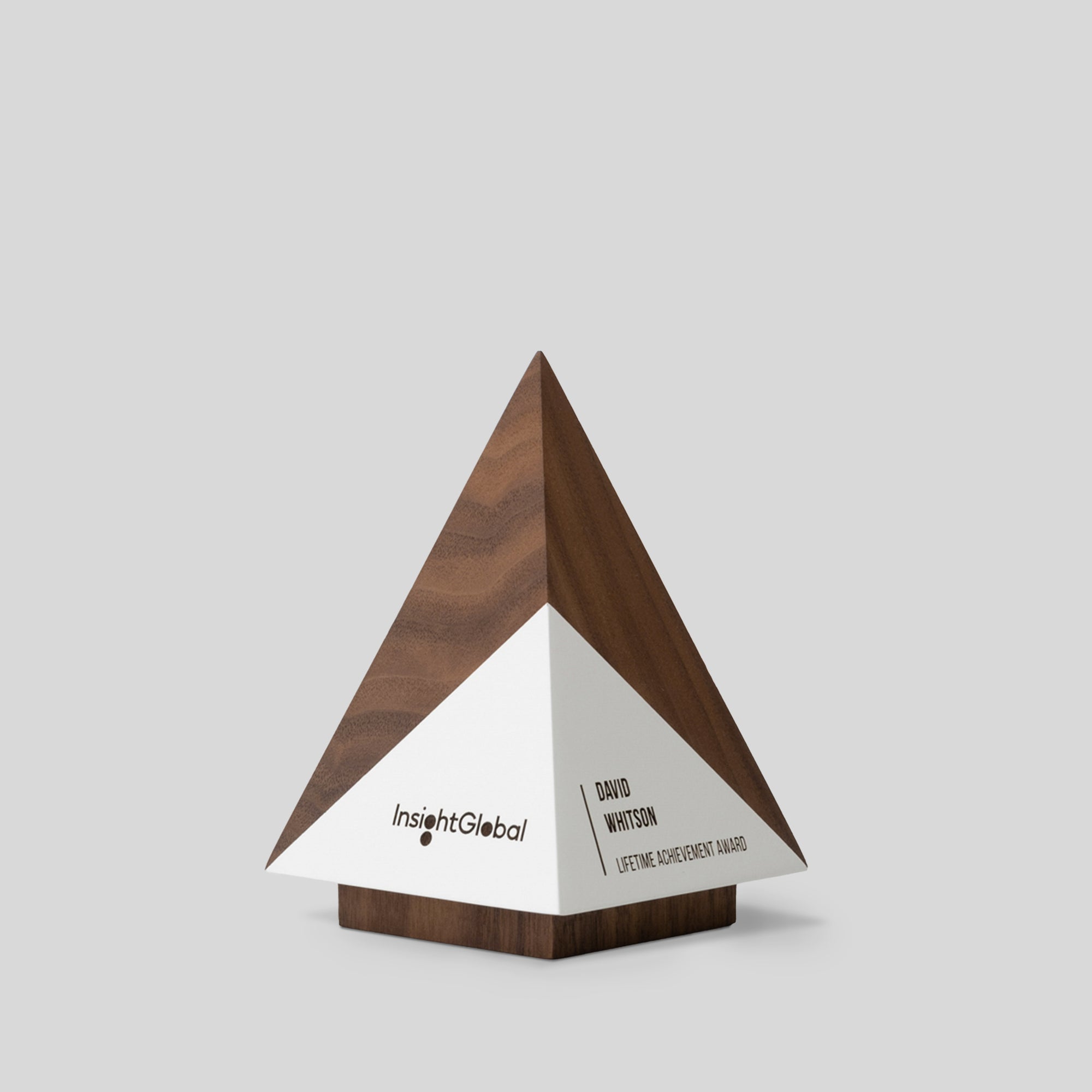 Geometria Award Pyramis, a wooden and white triangular sculpture, symbolizes achievement with its minimalist design and solid wood construction, reflecting strength and elegance.
