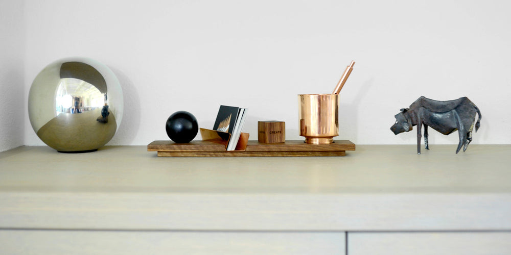 A styled interior tabletop scene with decorative objects including a large reflective metallic sphere, a black bull sculpture, a desk accessory in wood and copper with pen holder and engraved wooden plaque
