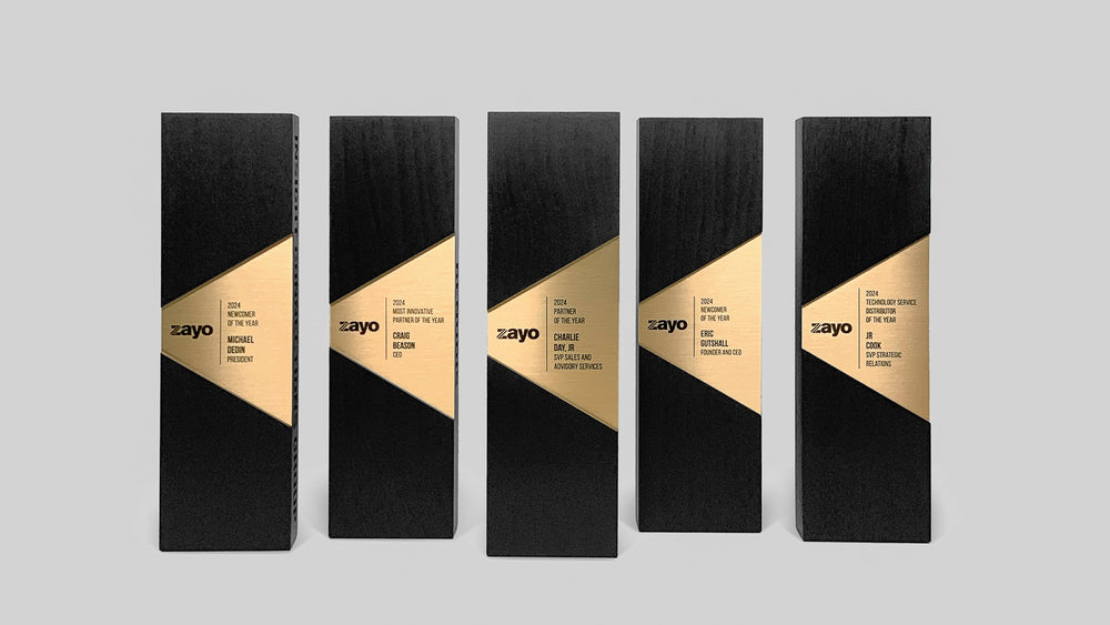 Custom Figura Trapezium Awards designed by Trophyology for Zayo’s partner recognition programs, featuring blackened walnut, brass nameplates, and bold geometric balance.