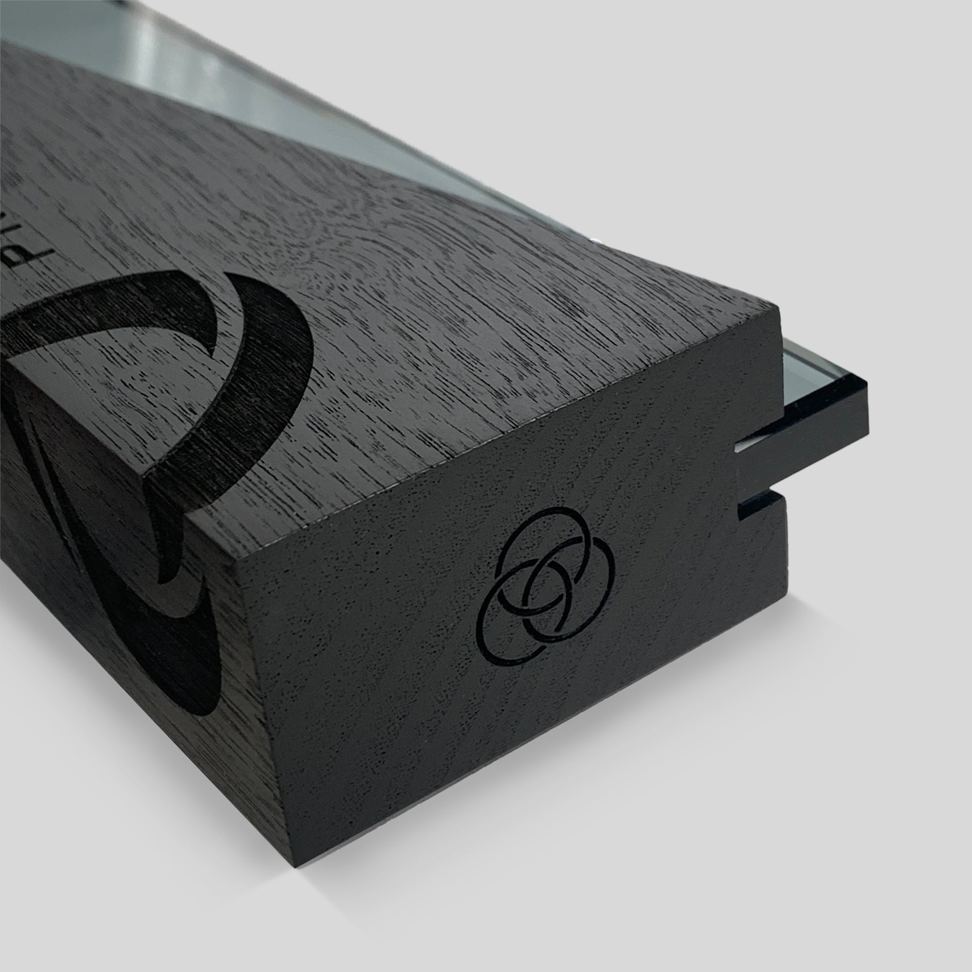 DI/MI Award: Close-up of ebony-stained wood featuring interlocking wood and glass trophy design elements that symbolize collaboration and creativity in a modern, sophisticated form, engraved for President's Club award trophies. 