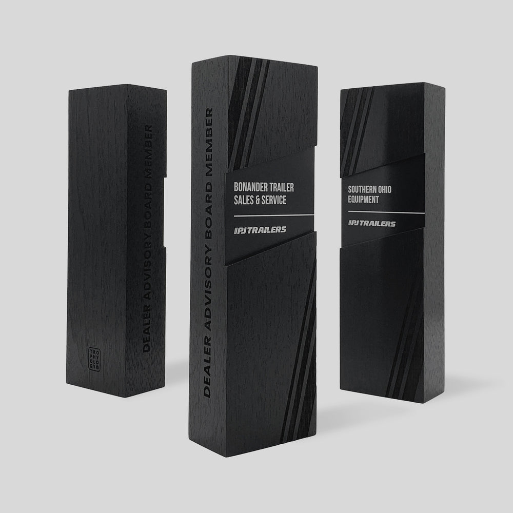 Figura Rectangulum Award, a black rectangular nameplate with white text, symbolizes leadership and balance, crafted with walnut and metals for a refined, modern look.