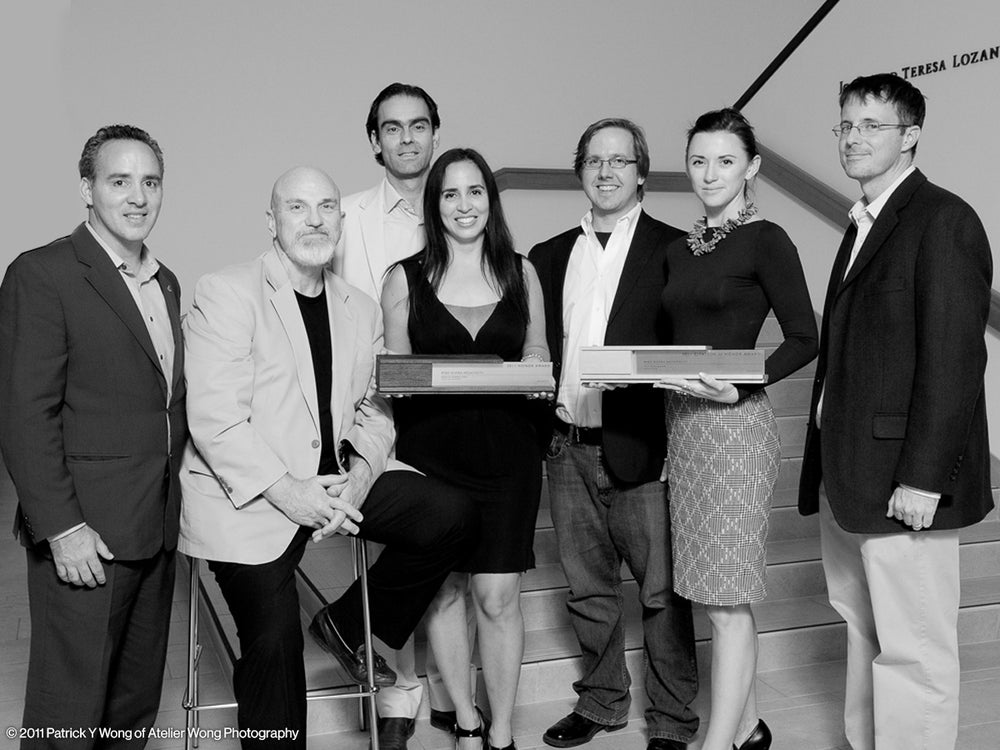 A group photo of seven architects in formal attire holding two executive recognition awards by Trophyology. 