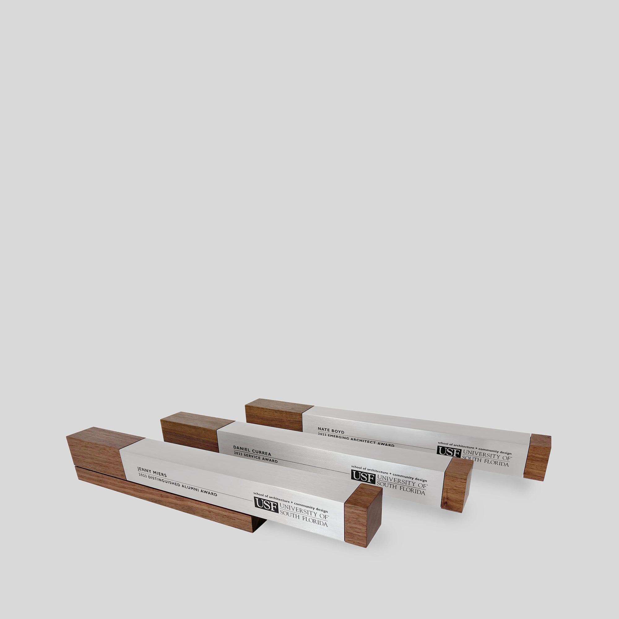 Fulgeo Award featuring a cantilevered aluminum beam on a walnut base, symbolizing innovation and success, displayed among other similar awards on a white surface.