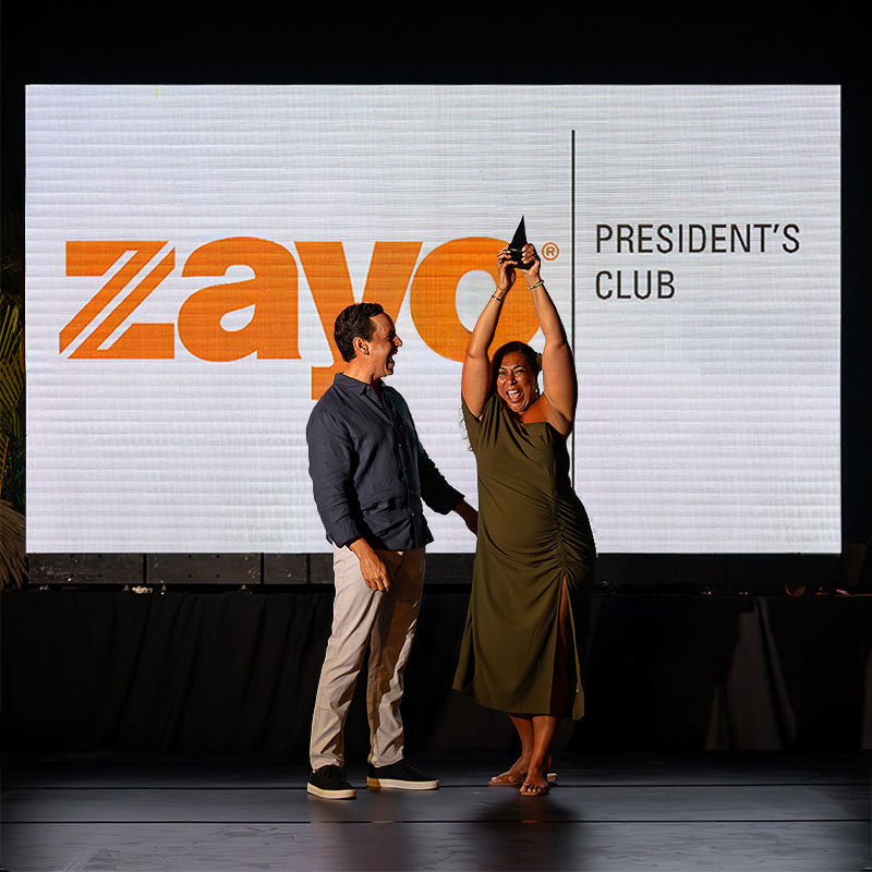 Zayo President’s Club honoree receiving her custom trophy on stage, displaying the Figura Trigonum design during the celebration ceremony.