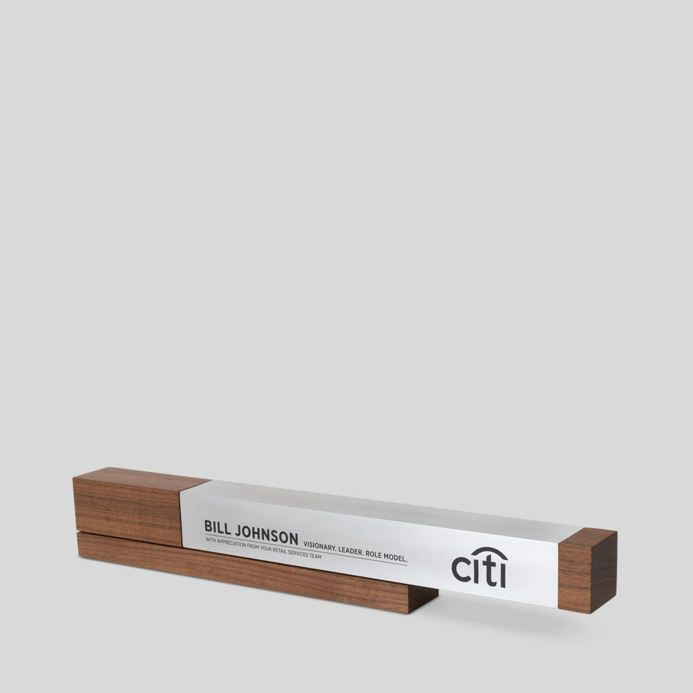 Fulgeo Award: A wooden block with a silver and black logo, featuring a cantilevered brushed aluminum beam on a finely-detailed walnut base, symbolizing innovation and stability.
